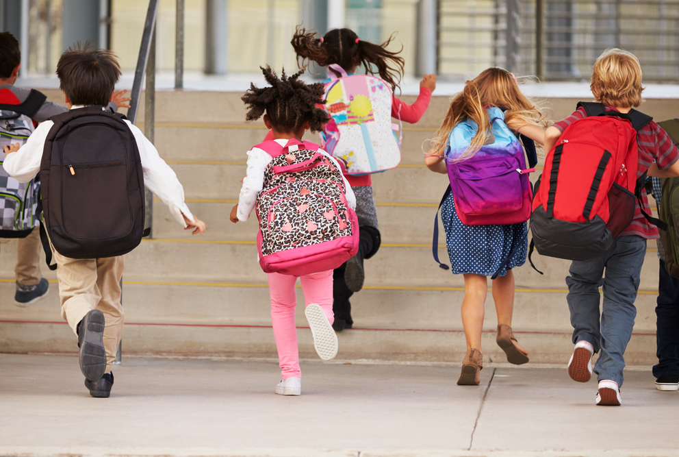 photo from behind of children with knapsacks running up stairs