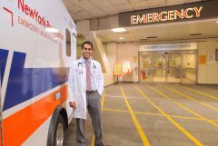a man smiling for a photo in front of an emergency room